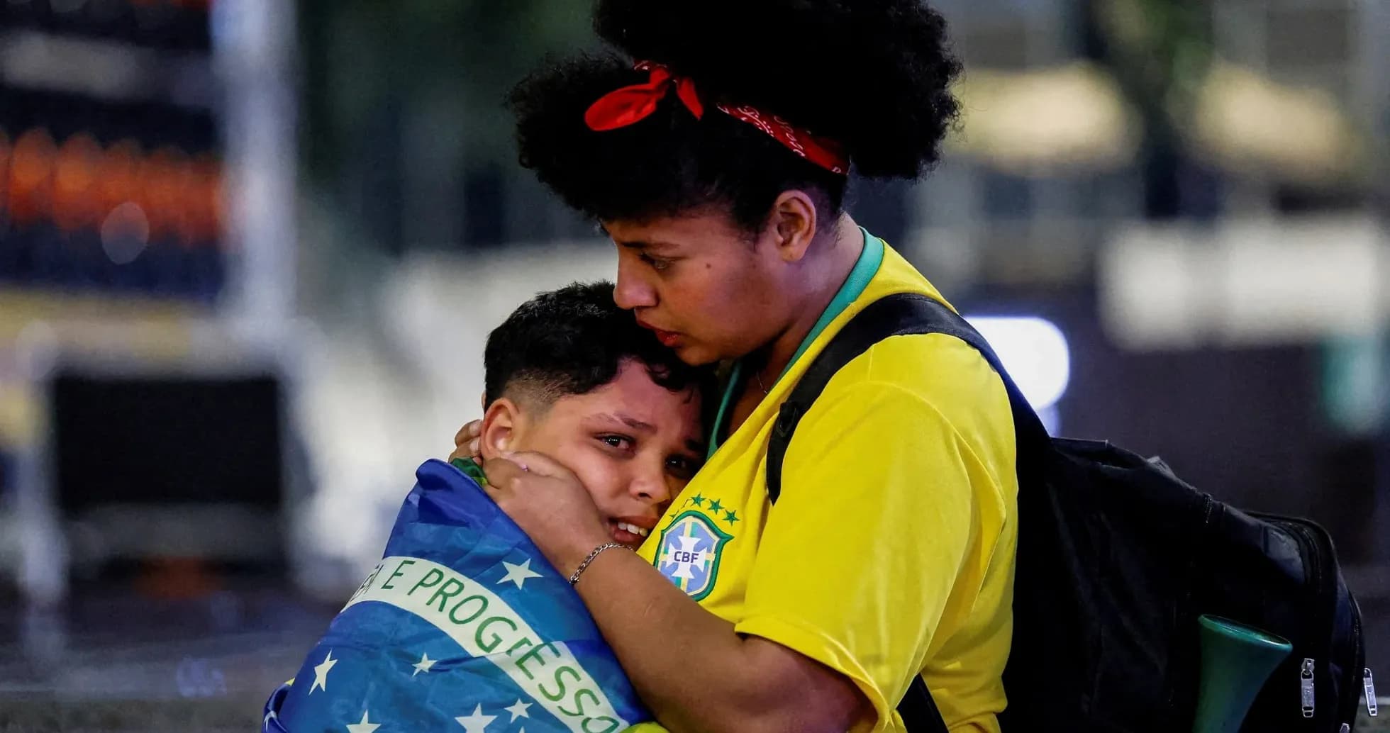 Mujer abraza a niño envuelto en bandera brasileña