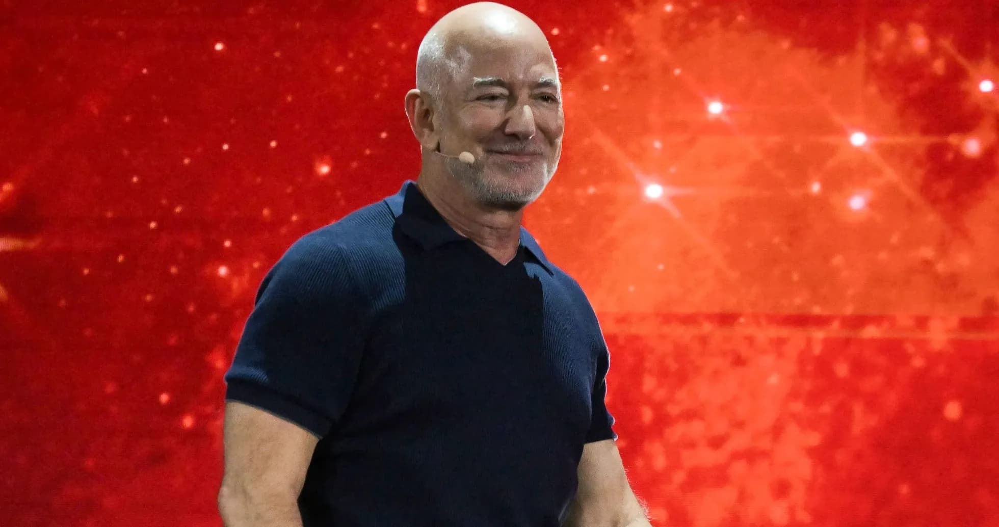 Hombre sonriente en un escenario con fondo rojo